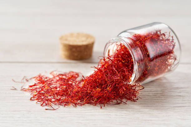 Dry saffron threads in a glass jar scattered on a white table. stock photo