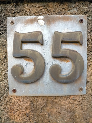 Fifty-five.55 in number on the wall of a house door, old bronze colored metal number.