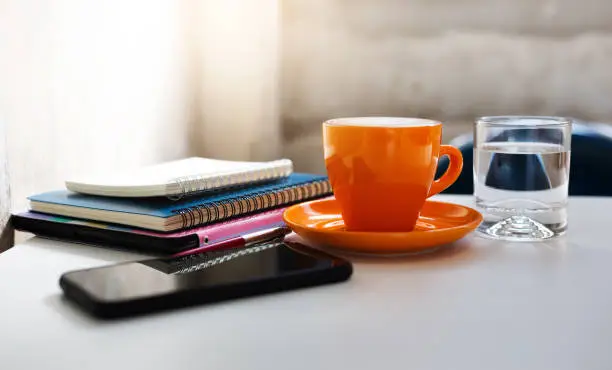 Close-up view, orange coffee cup with notebook placed on the tablet computer with smart phone and pen on table