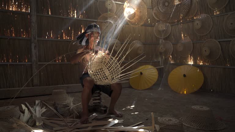 Asian village lifestyle, moment of process of a local male adult uncle basket weaver maker making bamboo basket and hat in a dry grass built room, very beautiful scenic 4k video