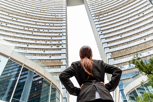 Young business woman in black suit stands at enterance of skyscraper