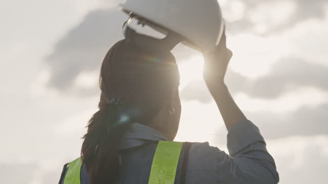 Slow motion of a female engineer talking off a construction helmet on at sunset
