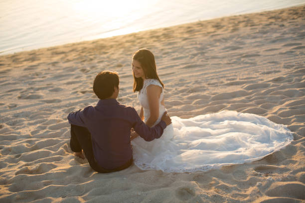 bride and groom sit on the sand