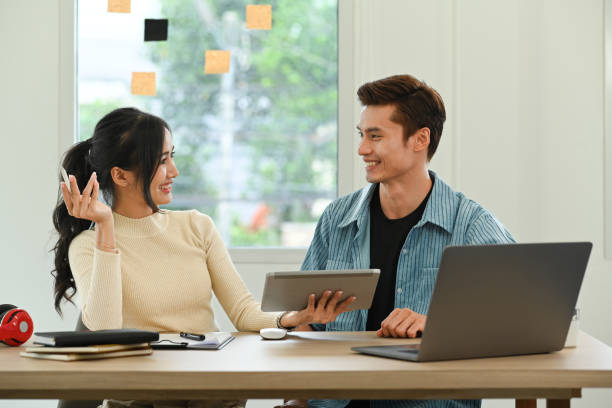istock Two smiling coworkers are discussing project, working together in modern creative office. 1449299298