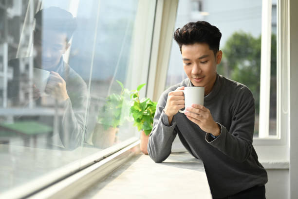 istock Handsome asian man enjoying his morning coffee while standing near office window overlooking cityscape. 1449299331