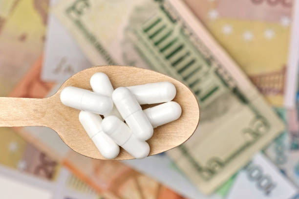 Pills in Wood Spoon on Paper Currency Background. Capsules, Vitamin with Money Cash. Expensive Drugs. Medical or Pharmacy Business, Finance Concept. Cost of Healthy Life. Medicine Price Backdrop. 4K . expensive píldoras en cuchara de madera sobre fondo de papel moneda. cápsulas, vitamina con dinero en efectivo. medicamentos caros. negocio médico o farmacéutico, concepto financiero. costo de la vida saludable. contexto del precio de los medicamentos. 4k
