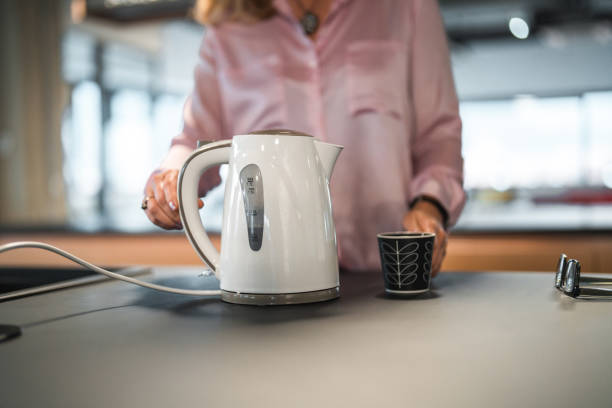 Caucasian Female Office Employee Using An Electric Kettle At Work stock photo