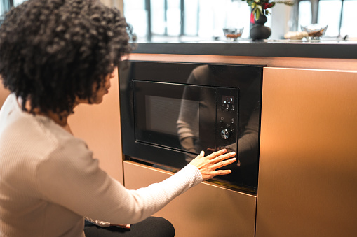 Hispanic female in 30s warming up her meal in a modern office using a microwave.