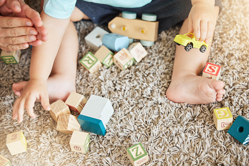 Closeup of baby learning with toys, block puzzle and train to help hand eye coordination on floor in home. Young child learn with education games on carpet, for cognitive development and fun in house