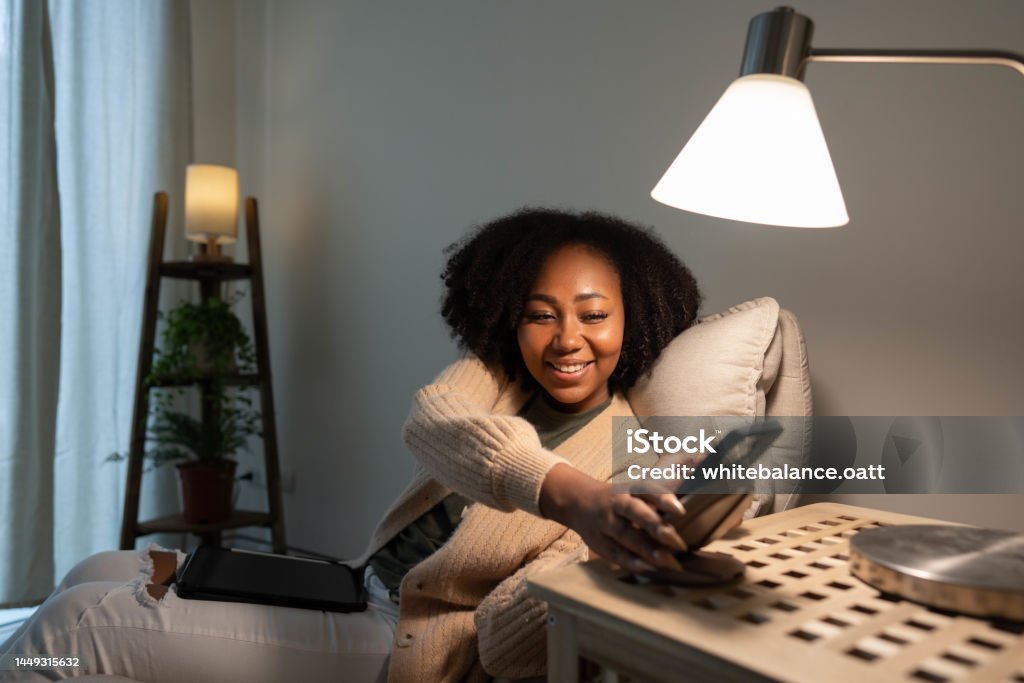 Woman putting her smartphone on wireless charger Young woman using mobile phone being placed on a modern wireless power bank. Lighting Equipment Stock Photo