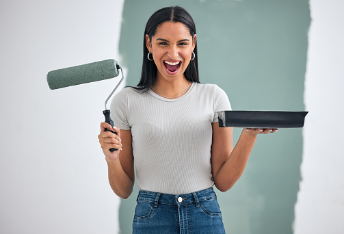 Home renovation, green paint and woman alone painting an interior wall of room with green paint. Home improvement, DIY creative project and paint roller in hand ready for exciting remodeling of house