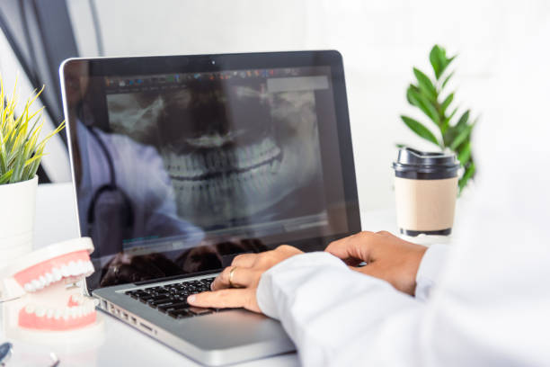 istock Dentist doctor or nurse in uniform use oral software teeth Xray and typing information medical history form into laptop 1449317148
