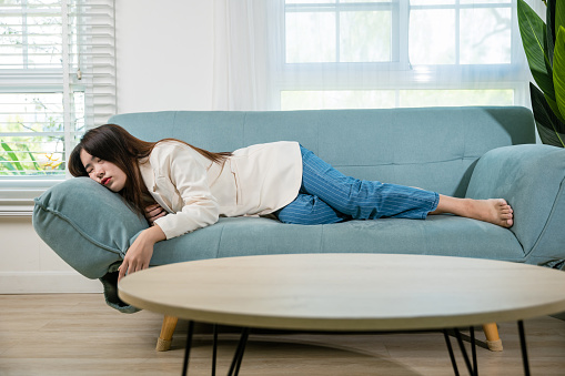 Tired woman sleeping closed eyes on sofa in living room at home after overworked working, Asian female resting falling asleep lying on couch, Full body