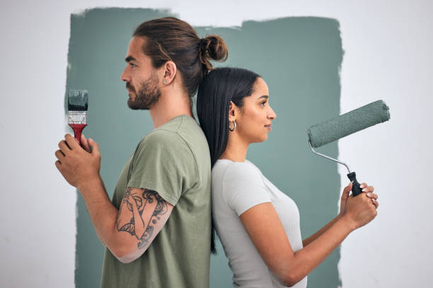paint, renovate and diy with a couple in their home for painting, redecorating or improvement. house, interior and room with a man and woman painting a wall in their apartment for renovation - female house painter home decorator paintbrush imagens e fotografias de stock
