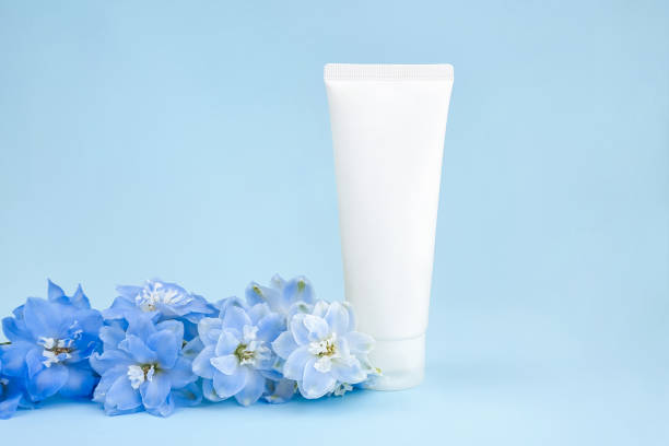 maqueta de tubo de plástico de botella de compresión blanca para la marca de medicamentos o cosméticos: crema, gel, cuidado de la piel, crema hidratante. envase de botella cosmética y flor azul de delphinium sobre fondo azul. vista frontal - human skin sparse washing face human face fotografías e imágenes de stock