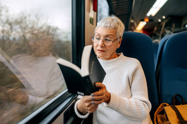 istock Senior woman enjoying a book while riding in a train 1449321279