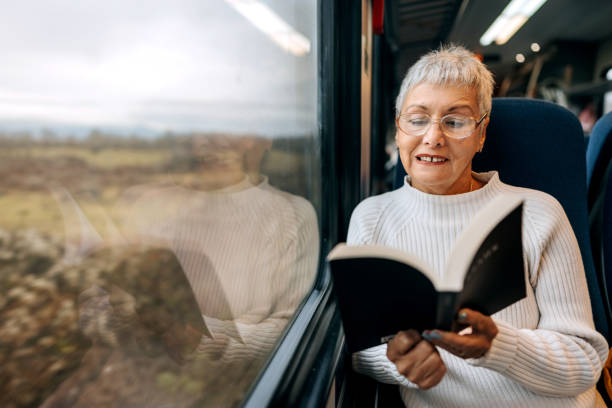 istock Senior woman enjoying a book while riding in a train 1449321386