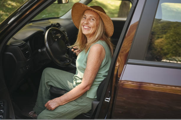 Excited senior woman sitting in new car outdoors holding keys, smiling, enjoying newly bought auto. Driving courses, insurance, road trip. Retired people activity. Happy female client car dealership. stock photo