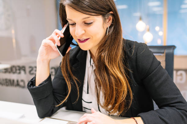 istock Young brunette executive girl in American jacket talking on the phone while looking at her laptop. Entrepreneur woman. 1449323159