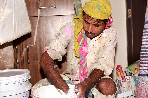 Painter mixing the paint in basket for house paint during Diwali festival sitting portrait at home.