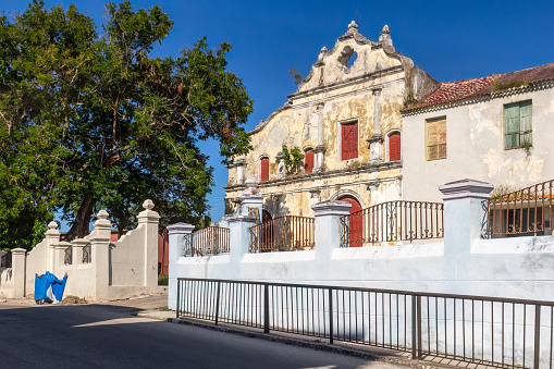 Havana, Cuba - October 24, 2022: The front facade of a church with a traditional concrete fence with wrought iron. A tree is in front of the church, and no people are on the scene.