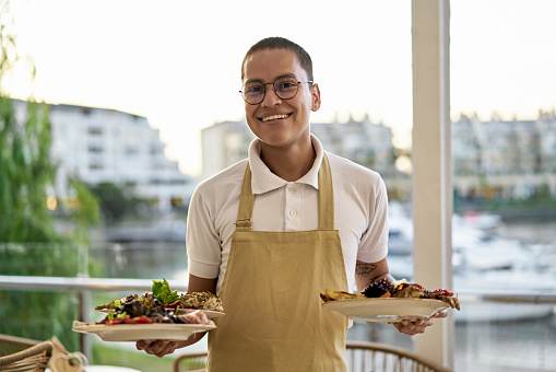 Waist-up view of shorthaired man in polo shirt, apron, and eyeglasses pausing to smile at camera.