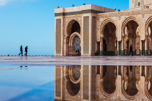 Casablanca, Morocco - January 28, 2018 : view of Hassan 2 mosque square reflected on water and two people walking