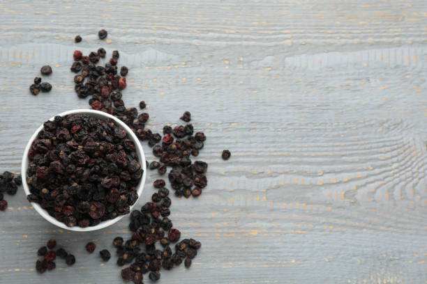 Dried black currants and bowl on grey wooden table, flat lay. Space for text