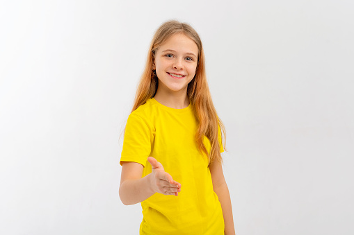 Beautiful adorable teen girl wearing casual yellow t shirt stands over white background, smiling friendly offering handshake as greeting and welcoming. Successful business