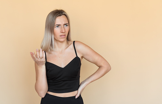 A Serious young woman with freckles gestures hand, looking frowning and thoughtful, stands over beige background