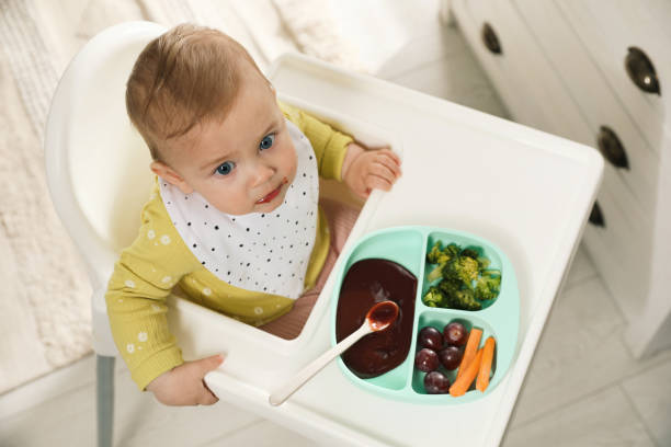 istock Cute little baby wearing bib while eating at home, above view 1449333633