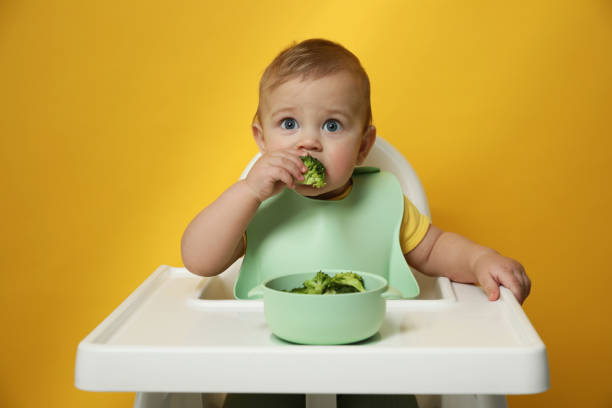 istock Cute little baby wearing bib while eating on yellow background 1449333655