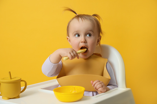 Lindo bebé con babero mientras come sobre fondo amarillo photo