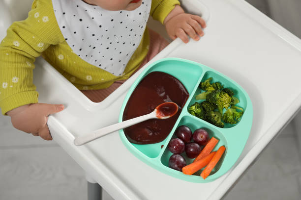 istock Cute little baby wearing bib while eating indoors, above view 1449334750