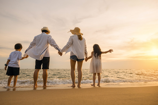 Back people enjoying travel trip and vacations, Silhouette of family father, mother, son and daughter holding hands together on beach, Happy family have fun jumping on beach in holiday at sunset