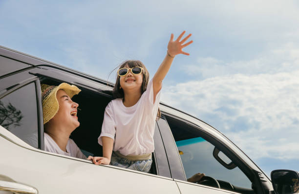 Pai da mãe asiática e filhos sorrindo sentados em um carro branco compacto olhando pelas janelas - foto de acervo