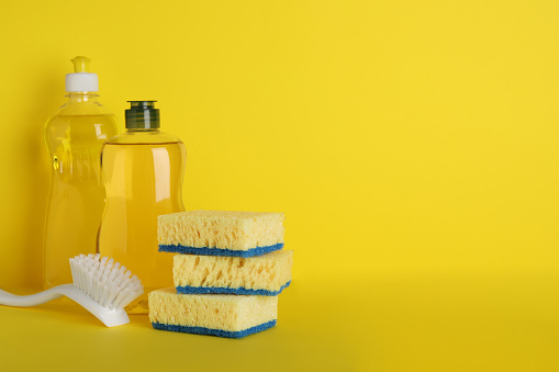 Sponges and other cleaning products on yellow background. Space for text