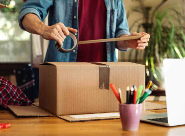 man sealing parcel with duct tape - returning imagens e fotografias de stock