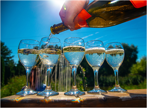 Hand pouring champagne from a bottle into a glass in sunlight.