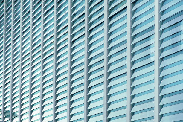 istock Perspective facade of modern minimalist glass fronted building with blue tones. Wall with a pattern of transparent overlapping glass of office building. Modern enclosed building with glass 1449342973