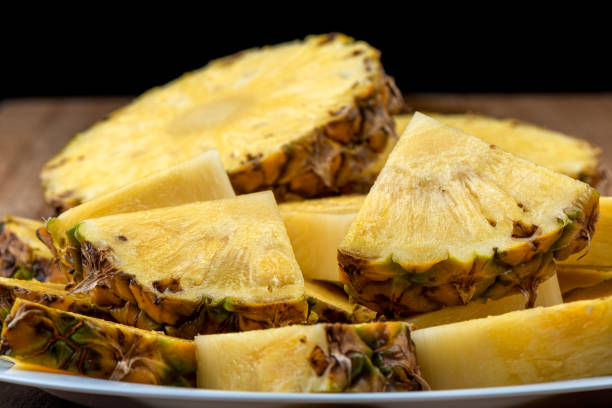 istock Sliced ripe pineapple on a white plate against a black background. 1449344793