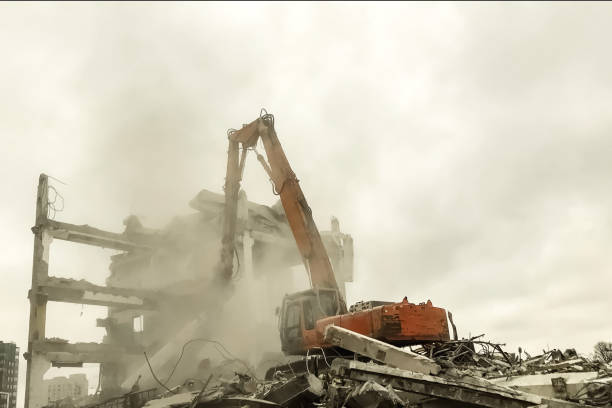 Hydraulic excavator surrounded with dust cloud taking down an old building at cloudy sky background. House demolition with heavy machinery on construction site. Renovation concept. Copy text space
