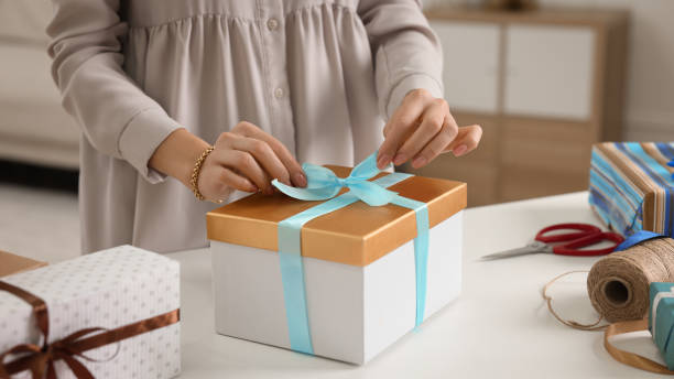 istock Woman decorating gift box with ribbon at white table indoors, closeup 1449346980