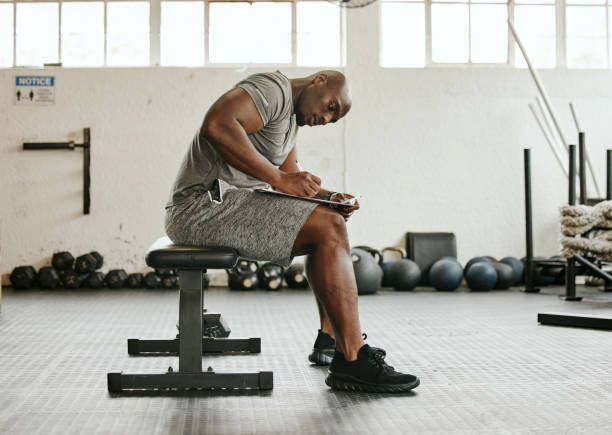 istock Gym membership, personal trainer and black man writing on clipboard for exercise, training or workout schedule and program. Male sports coach working on health, wellness and fitness plan or goals 1449348255