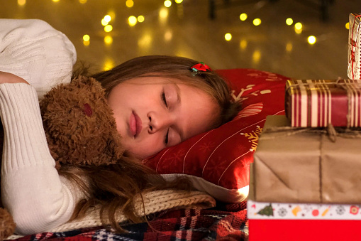 Little girl at Christmas Eve sleeping waiting for gift for holiday from Santa Claus. Traditional family celebration, childhood and children dreams