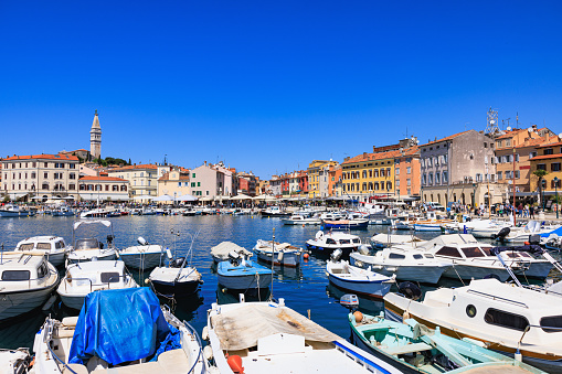 Motor boats anchored in Rovinj marina floating on sea surface, townscape accross the bay