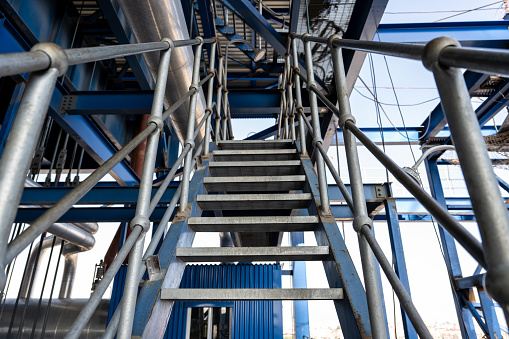 frontal view of a steel spiral staircase in industrial design leading upwards next to a brick facade in a modern backyard outside of an office building