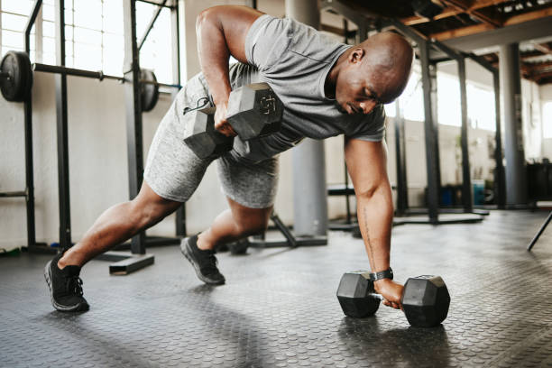 haltère, fitness et culturiste homme noir avec entraînement dans la salle de sport ou le studio de garage pour le bien-être, l’objectif corporel et la motivation. homme de sport puissant, fort et africain faisant de l’exercice de push up avec de l� - muscular build wellbeing exercise equipment instructor photos et images de collection