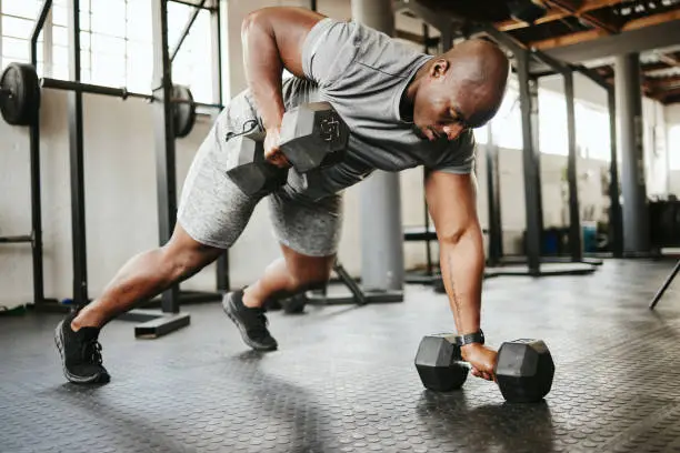 Photo of Dumbbell, fitness and bodybuilder black man with workout training in gym or garage studio for wellness, body goal and motivation. Power, strong and african sports man doing push up exercise with gear