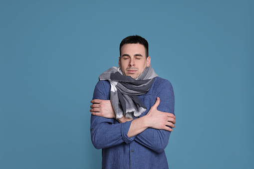 Young man with scarf suffering from fever on blue background. Cold symptoms